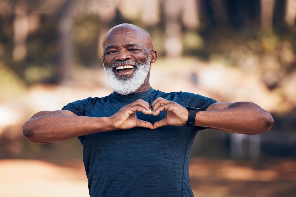 Portrait, heart health fitness and senior man self care, cardiology and workout health support in forest or outdoor running. Face of sports person with retirement love hands in the woods or nature wellness